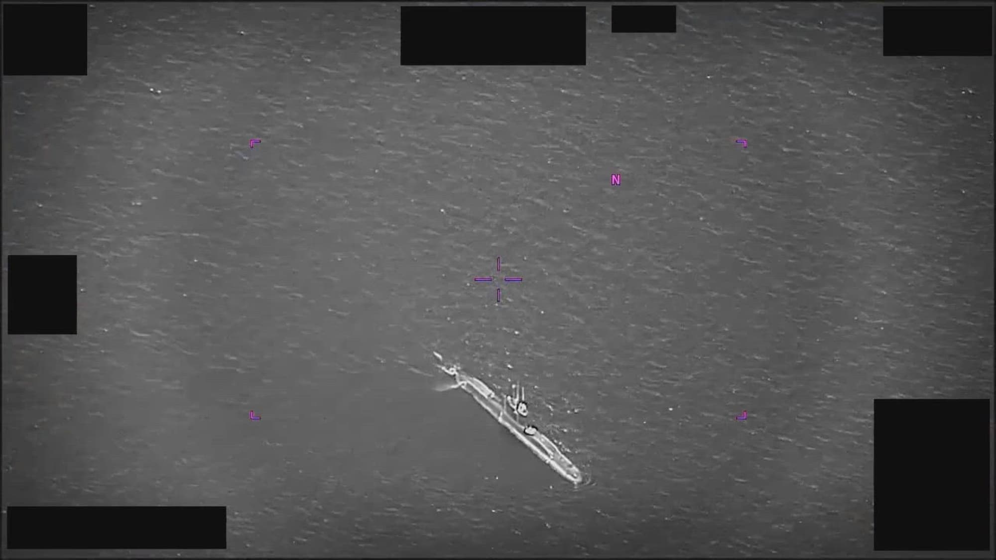 DOW-UAP-PR067 — U.S. submarine surfaced in the moment of the March 25, 2022 multi-USO transmedium encounter. Magenta tactical HUD overlay marks the targeting reticle; redaction blocks frame the edges. Released by the Department of War in PURSUE Release 02.