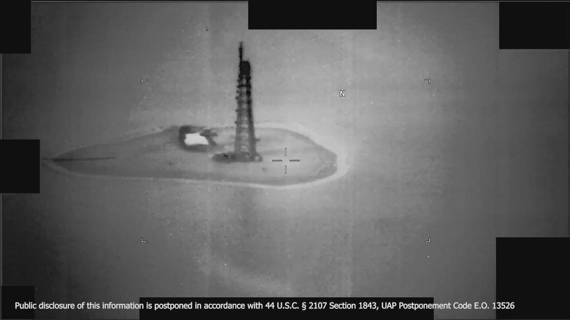 DOW-UAP-PR135 — a frame from a U.S. Central Command infrared sensor video in the Middle East in 2025, showing a lattice tower on a small island under the sensor's reticle. The accompanying Mission Report describes six small spherical objects grouped together, frequently changing direction, at an estimated 480 miles per hour.